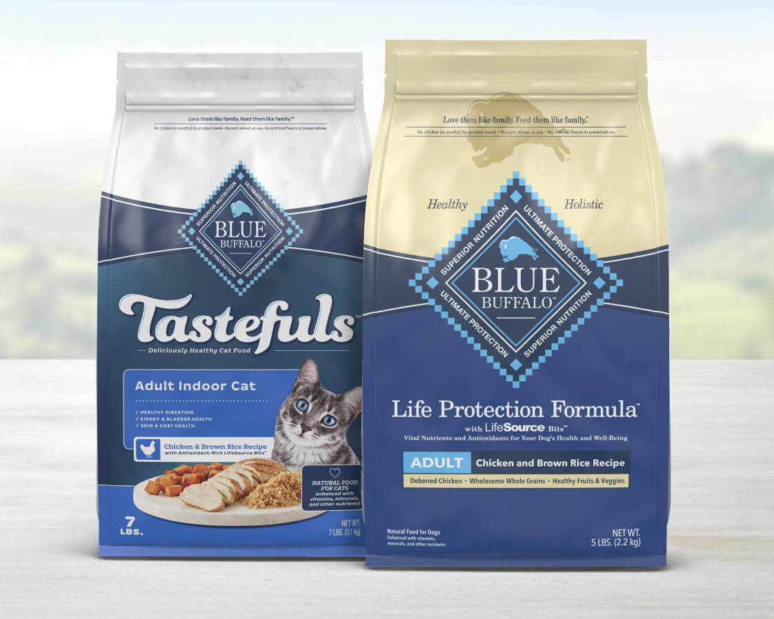 Two bags of Blue Buffalo pet food on a table with a window view; one labeled 'Tastefuls' for cats and the other 'Life Protection Formula' for dogs. Both are chicken and brown rice recipes.
