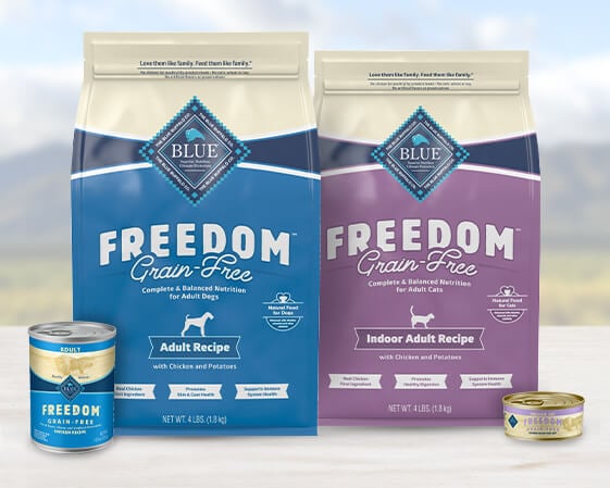 Two bags and two cans of Blue Freedom Grain-Free pet food for cats and dogs displayed on a surface.