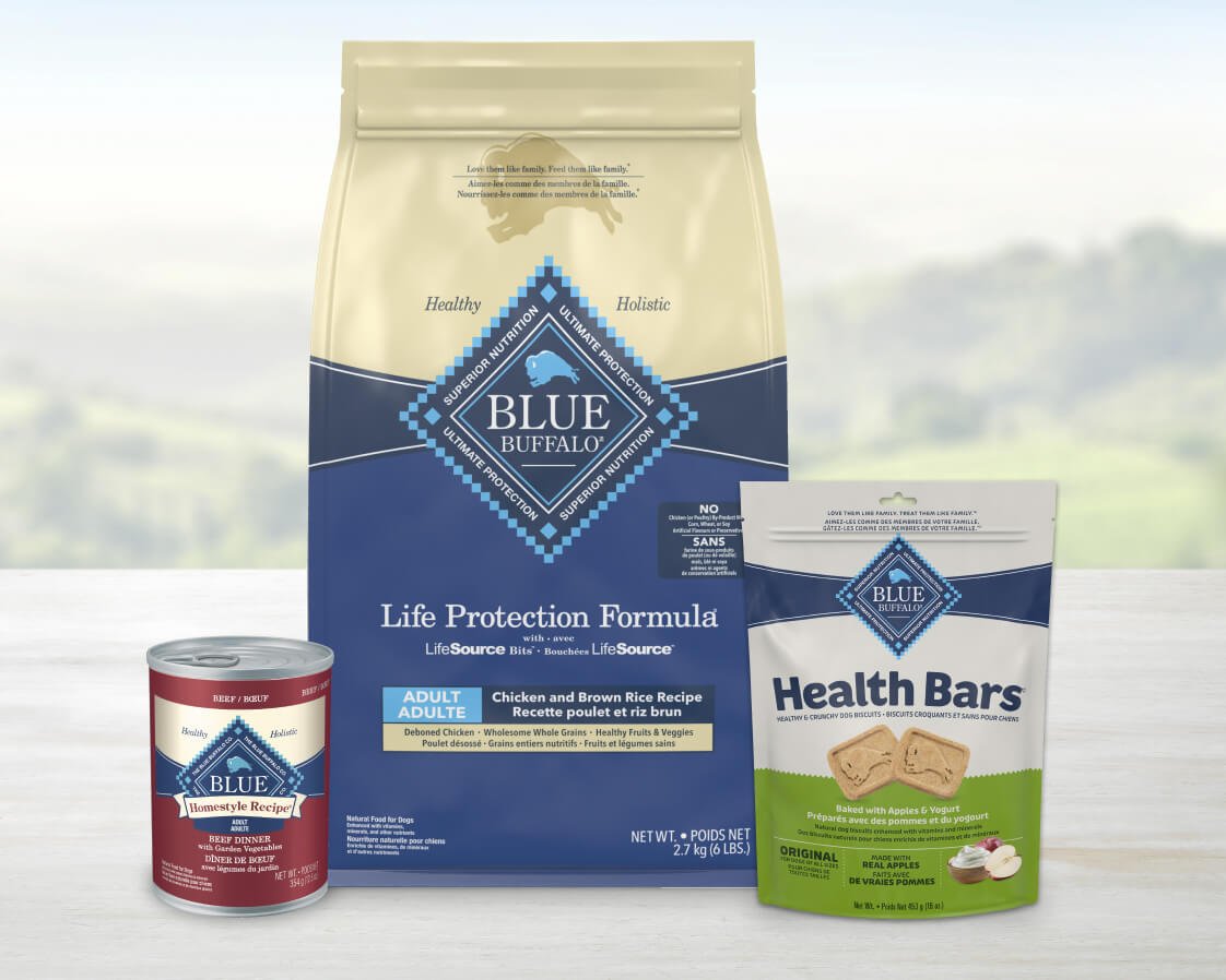 A range of Blue Buffalo pet food products, featuring dry dog food, canned wet food, and dog treats against a soft, natural background.