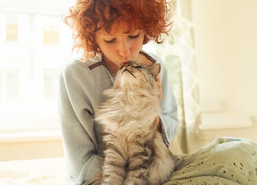 A young woman affectionately holds her cat and kisses the top of their head.