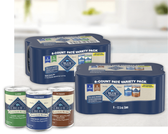 Three cans of wet dog food are placed beside an unopened multipack box featuring the same recipes.