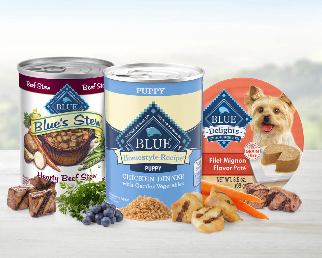 Selection of Blue brand pet food products, including cans and a patÃ©, displayed with ingredients like meat and vegetables.