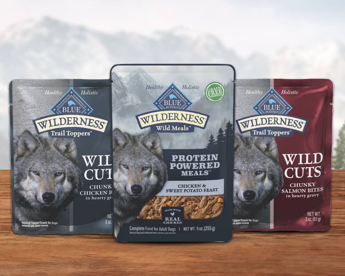 Two pouches of Wilderness Trail Toppers Wild Cuts and a pouch of Wilderness Wild Meals are on a wooden counter.