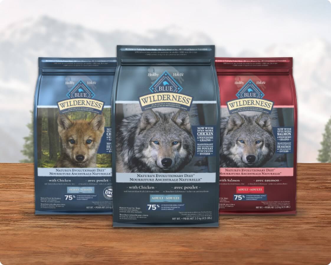 Three bags of Wilderness dog food in blue, dark blue, and red packaging, each featuring a wolf.