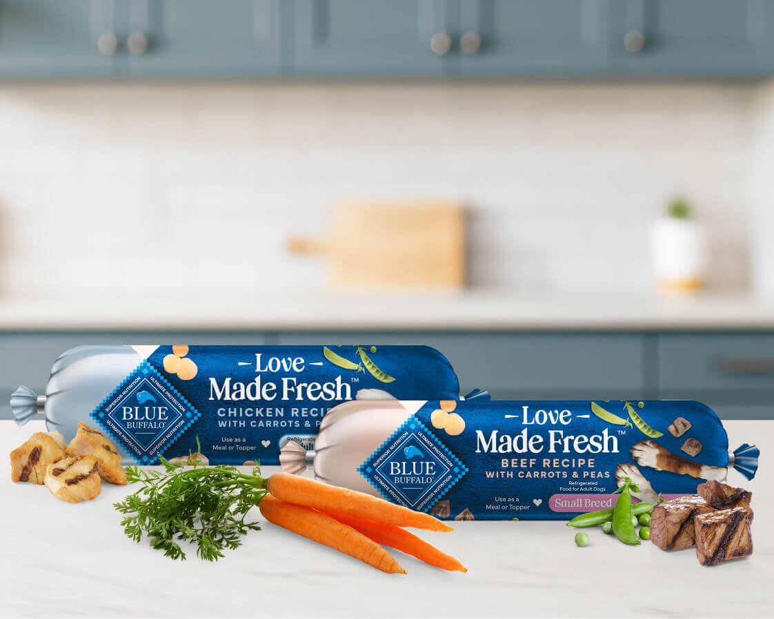 Two rolls of Love Made Fresh dog food are surrounded by fresh parsley, peas, carrots, and bits of seared chicken and beef.