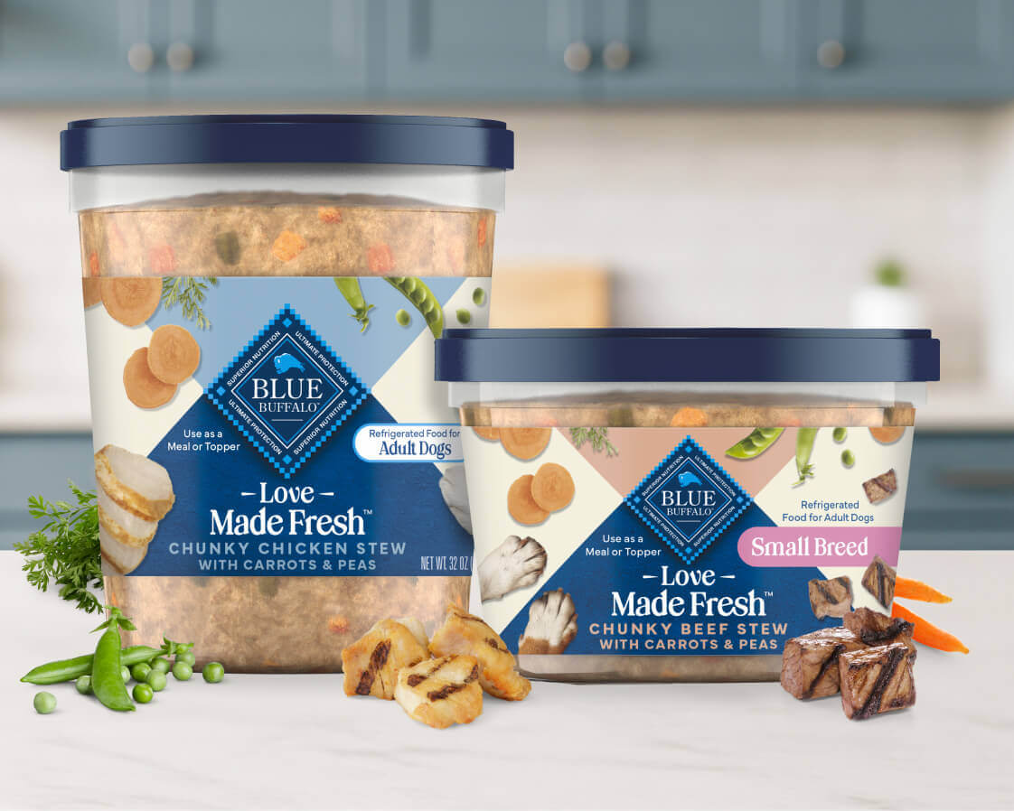 Two tubs of Love Made Fresh dog food are surrounded by fresh parsley, peas, carrots, and bits of seared chicken and beef.