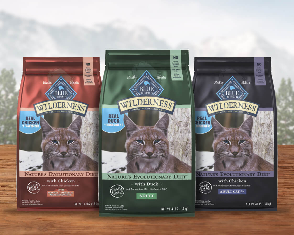 Three bags of BLUE Wilderness cat food labeled with chicken, duck, and salmon flavors. A bobcat image is on each bag.