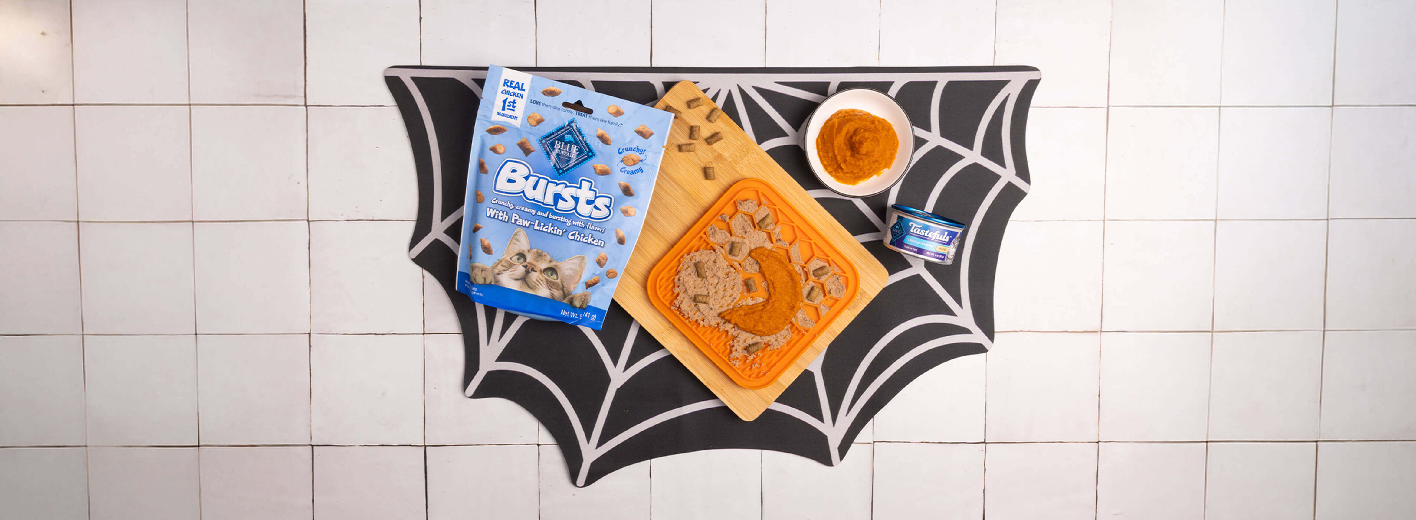 The recipe on a spider web placemat w/a lick mat, a half moon-shaped bowl, a spatula, & a bowl of Tastefuls cat food