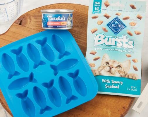 Packaging and mold for Blue Buffalo Bursts cat treats with a seafood flavor, beside a can of Tastefuls cat food, displayed on a kitchen counter.