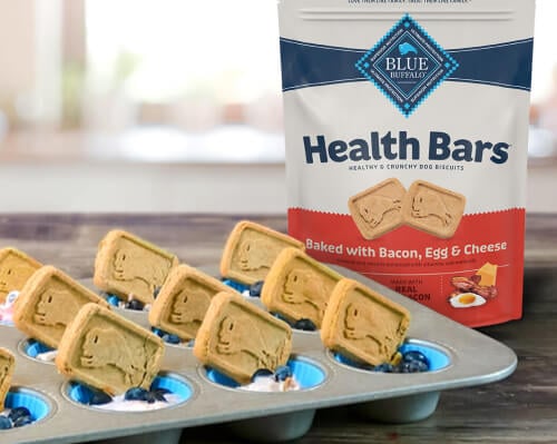 Blue Buffalo Health Bars Bacon, Egg & Cheese dog biscuits in a muffin tin with blueberries.