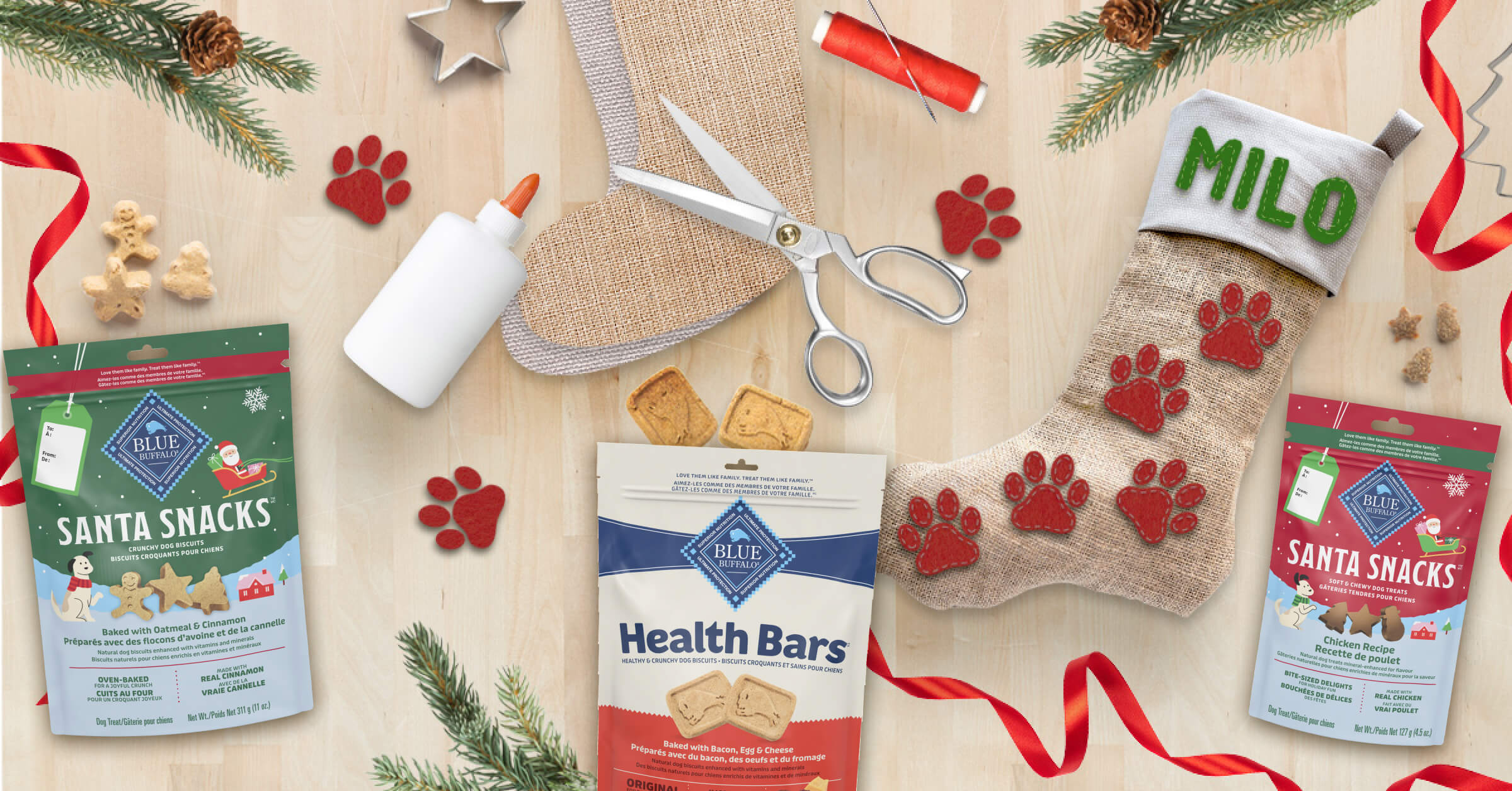 Dog treat packages, stocking labeled 'MILO', scissors, glue, and holiday decor on table.