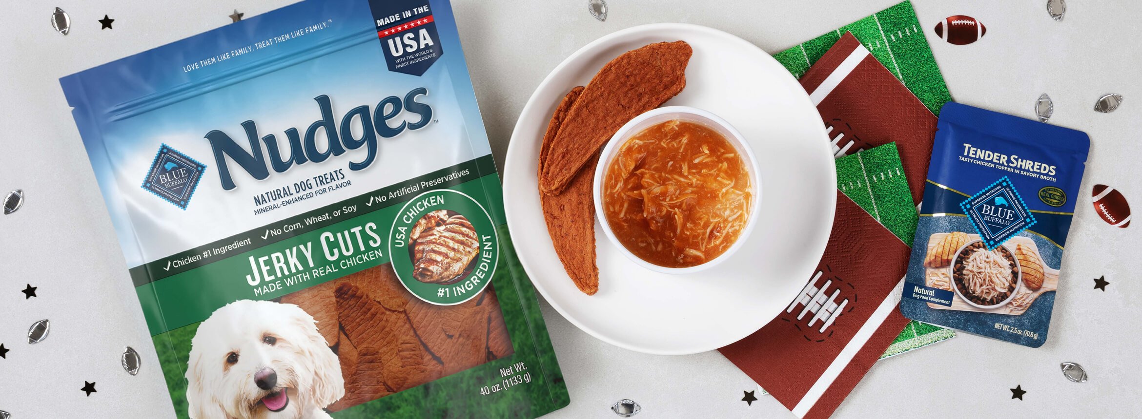 A bag of Nudges dog treats, a bowl of shredded chicken, and football-themed napkins sit on the table.
