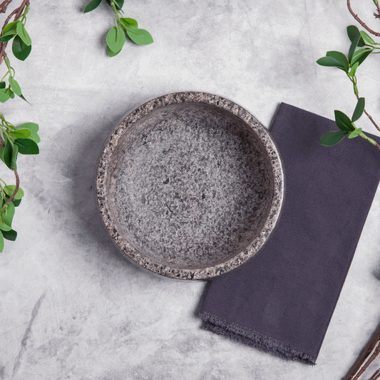 Stone bowl filled with guacamole surrounded by tortilla chips, green leaves, and a dark napkin on a light surface.