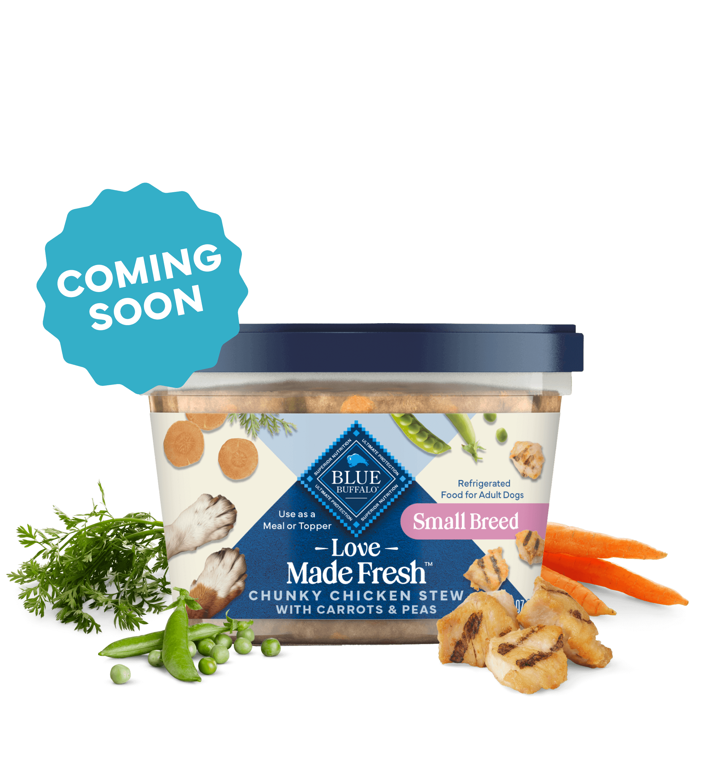 A tub of Love Made Fresh chicken stew is surrounded by parsley, chunks of seared chicken, carrots, and peas on a countertop.