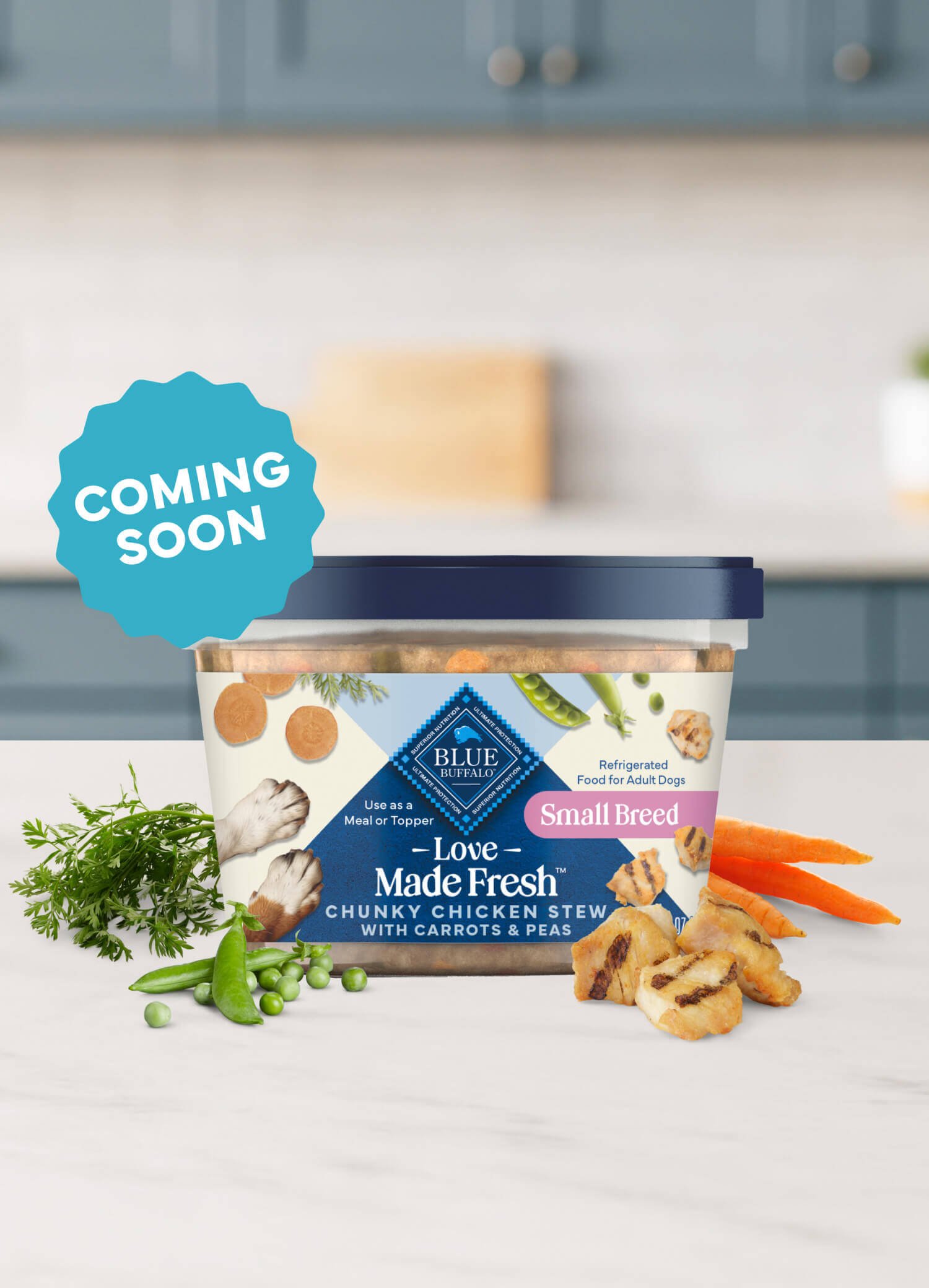 A tub of Love Made Fresh chicken stew is surrounded by parsley, chunks of seared chicken, carrots, and peas on a countertop.