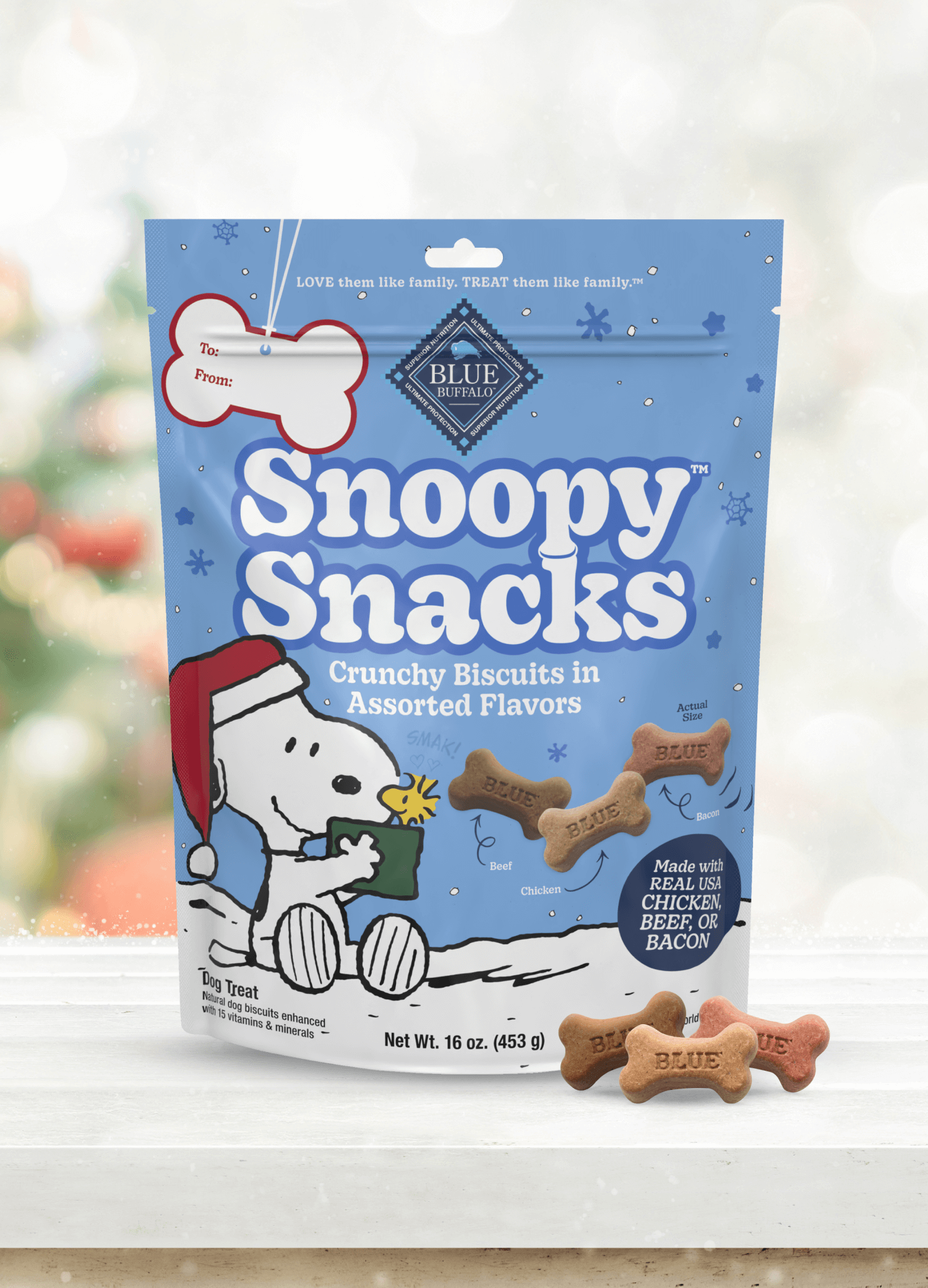 A small bag of BLUE Snoopy Snacks on a windowsill with a softly blurred Christmas tree in the background. Three Snoopy Snacks are neatly stacked in front of the bag.