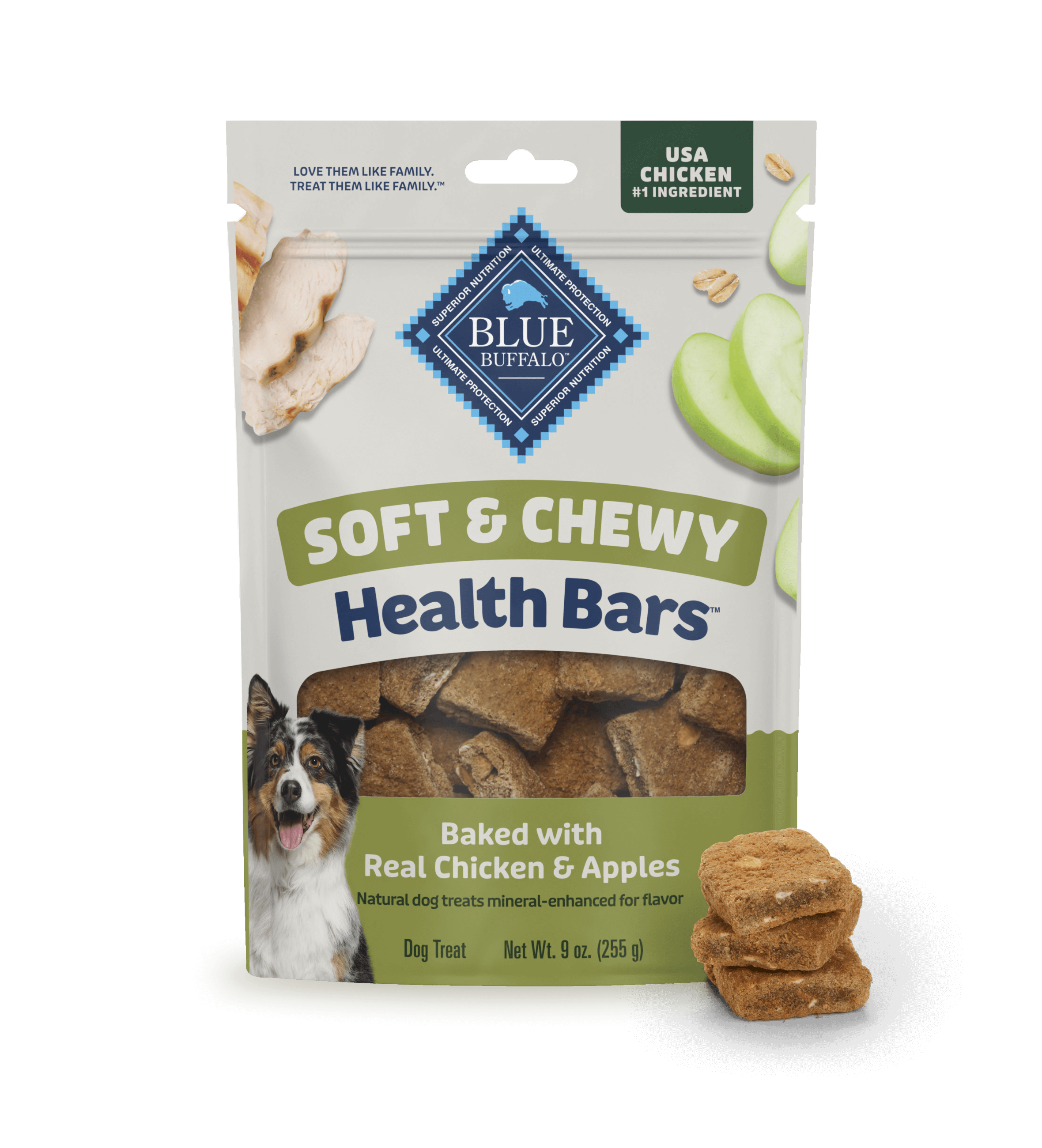 A bag of BLUE dog treats sits on a light surface against a blue-and-white background. The package shows crispy, sliced apples, pieces of juicy tender chicken, and a happy dog. A small stack of treats sits beside the treat bag.