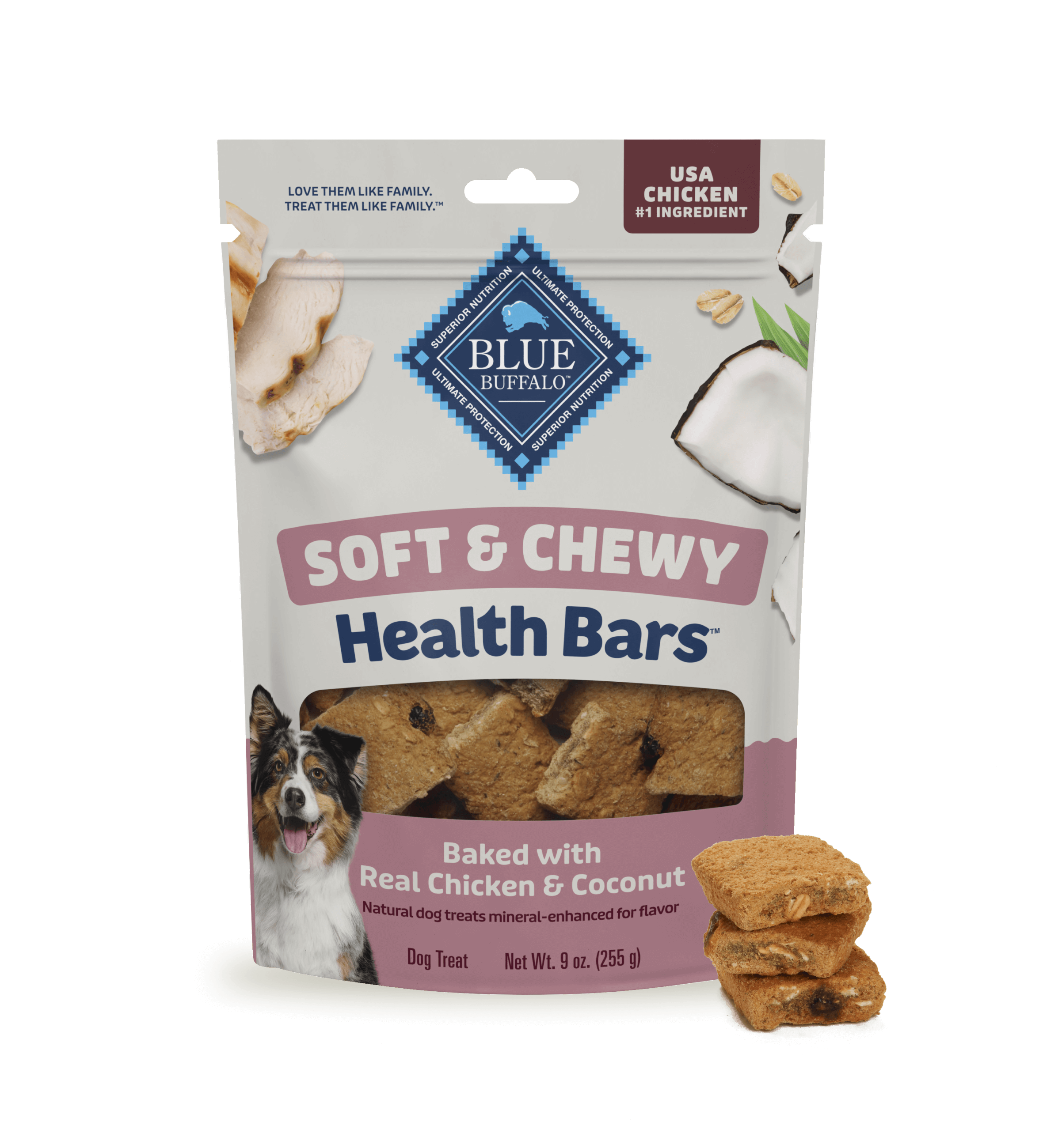 A bag of BLUE dog treats sits on a light surface against a blue-and-white background. The package shows fresh coconut, pieces of tender, juicy chicken, and a happy dog. A small stack of treats sits beside the treat bag.