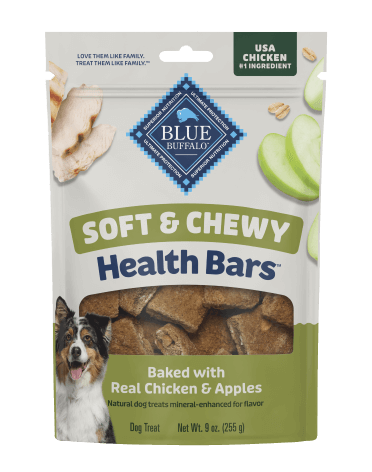  A package of BLUE dog treats shows crispy, sliced apples, pieces of juicy tender chicken, and a happy dog. A small stack of treats sits beside the treat bag.