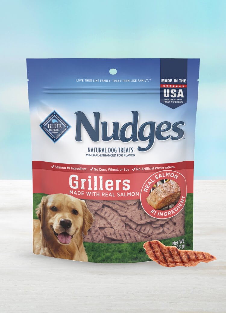 A pack of BLUE Nudges Grillers Salmon Recipe dog treats with one Nudges Griller treat in front of the pack