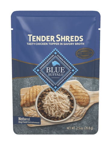 Pouch of Tender Shreds chicken dog food topper with shredded chicken and kibble on a wooden board.